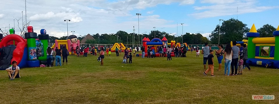 Niños con sus padres jugando en distintos brincolines inflables en un campo de deportivo.